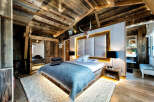 Experience rustic luxury in this stunning chalet bedroom, featuring a king-sized bed with a plush blue throw and a striking upholstered headboard.