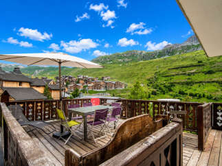 Enjoy breathtaking mountain views from this charming chalet's private balcony, complete with outdoor seating and a large umbrella for shade.