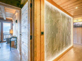 Experience rustic luxury in this mountain chalet, featuring natural wood finishes and a striking stone accent wall illuminated by soft, ambient lighting.