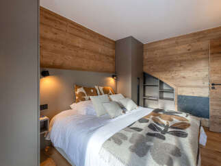 Experience cozy mountain living in this charming bedroom featuring rustic wood-paneled walls and a comfortable bed adorned with plush pillows and a decorative throw.