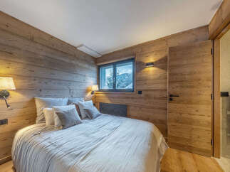 Experience cozy mountain living in this charming bedroom featuring warm, wood-paneled walls and a comfortable bed adorned with plush pillows.