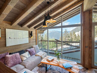 Experience breathtaking mountain views from this stunning living room, featuring a large picture window and a cozy sectional sofa.