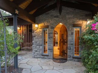 Step into a charming stone cottage featuring a grand arched wooden door, flanked by elegant windows.