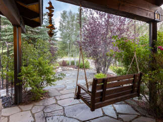 Enjoy the serene outdoors from this charming porch swing, perfect for relaxing amidst lush greenery.