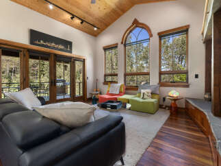 Experience breathtaking mountain views from this stunning living room, featuring a vaulted wood-paneled ceiling and a dramatic arched window.