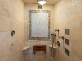 Experience luxury and accessibility in this custom-tiled shower featuring a built-in wooden bench for ultimate comfort.