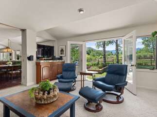 Experience breathtaking mountain views from this inviting living space, featuring comfortable blue leather recliners and direct access to a lush outdoor landscape.