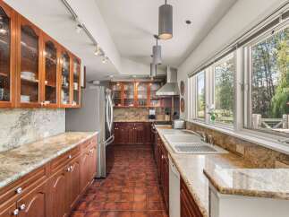 Discover this charming kitchen featuring rich cherry wood cabinetry with glass-front upper cabinets, complemented by elegant granite countertops and a classic tile backsplash.