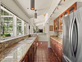 This spacious kitchen boasts ample natural light streaming through large windows, illuminating the granite countertops and rich wood cabinetry.