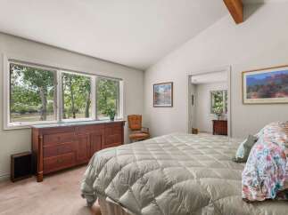 Experience serene living with this charming bedroom featuring a large dresser and expansive windows that offer breathtaking views of the surrounding nature.