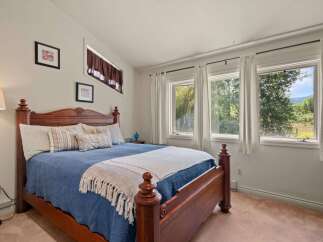 Experience serene mountain living in this charming bedroom, featuring a cozy queen-size bed adorned with a beautiful blue quilt and a decorative throw.