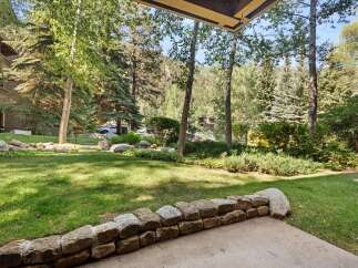 Enjoy the serene mountain setting from this charming property, featuring a lush green lawn and a picturesque stone wall.