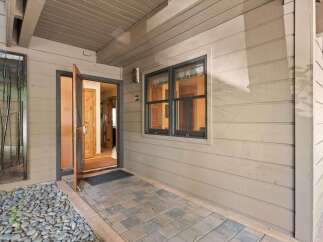 Welcome guests into this charming home through a welcoming entryway featuring a light-colored stone pathway leading to an open wooden door.