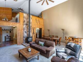 Experience rustic charm in this spacious living area featuring a striking stone fireplace and warm wood paneling.