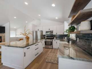 Experience modern living in this stunning kitchen, featuring sleek white cabinetry, a spacious island with a captivating marble countertop, and a sophisticated dark tile backsplash.