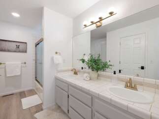 This bright and airy bathroom features a double vanity with white tile countertops and brass fixtures, perfect for a busy household.