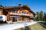 Experience luxury mountain living in this stunning wooden chalet, featuring a spacious balcony with intricate wooden railings and expansive windows that invite natural light.