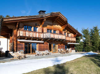 Experience luxury mountain living in this stunning wooden chalet, featuring a spacious balcony with intricate wooden railings and expansive windows that invite natural light.