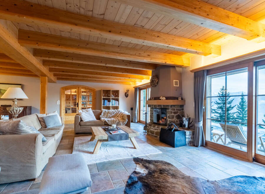 Experience rustic luxury in this stunning mountain chalet living room, featuring a grand stone fireplace and exposed wooden beams.