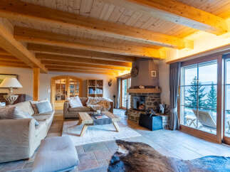 Experience rustic luxury in this stunning mountain chalet living room, featuring a grand stone fireplace and exposed wooden beams.