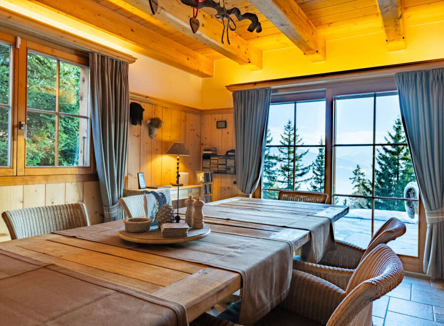 Experience cozy mountain living in this charming dining room, featuring a rustic wooden table set for a meal and surrounded by comfortable wicker chairs.