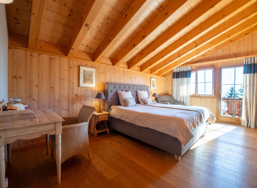 Experience rustic charm and modern comfort in this beautifully appointed bedroom, featuring warm wooden paneling and a vaulted ceiling with exposed beams.