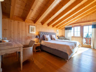 Experience rustic charm and modern comfort in this beautifully appointed bedroom, featuring warm wooden paneling and a vaulted ceiling with exposed beams.