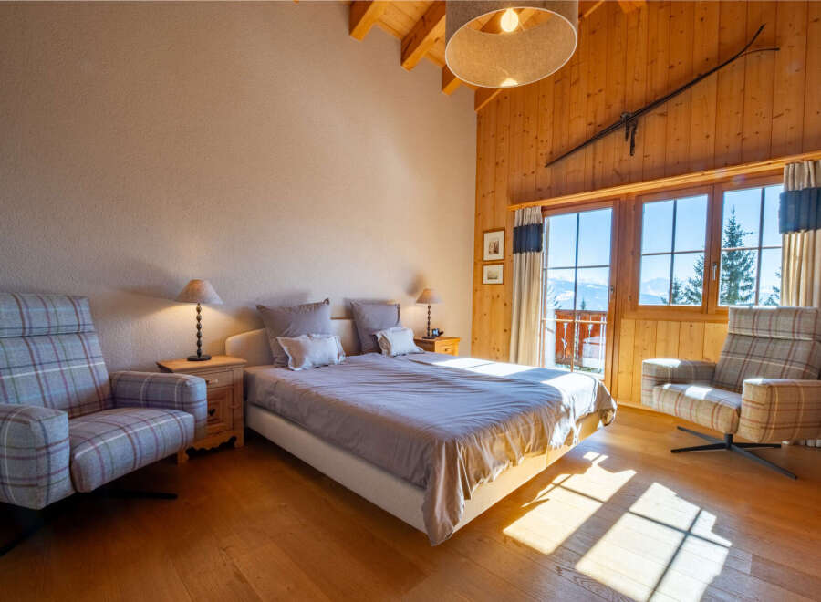 Experience cozy mountain living in this charming bedroom featuring a comfortable bed, plush armchairs, and a rustic wooden ski decor.