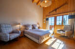Experience cozy mountain living in this charming bedroom featuring a comfortable bed, plush armchairs, and a rustic wooden ski decor.
