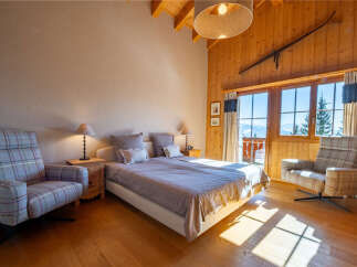Experience cozy mountain living in this charming bedroom featuring a comfortable bed, plush armchairs, and a rustic wooden ski decor.