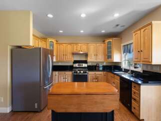 This spacious kitchen features beautiful light wood cabinetry complemented by sleek black granite countertops.