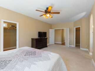 This spacious bedroom features a large dresser with a television, a ceiling fan for comfort, and ample closet space.