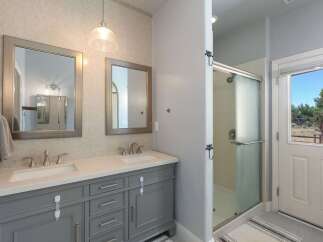 This modern bathroom features a spacious double vanity with sleek gray cabinetry and quartz countertops, complemented by two elegant framed mirrors.