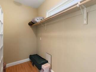 Discover ample storage solutions in this spacious walk-in closet, featuring a convenient built-in shelving unit on the left and a sturdy wooden rod with a shelf above for hanging clothes and storing items.