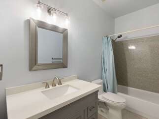 This modern bathroom features a sleek vanity with a white countertop and a brushed nickel faucet, complemented by a large framed mirror and a stylish vanity light fixture.