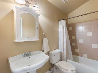 This charming bathroom features a classic pedestal sink with a chrome faucet, complemented by a white medicine cabinet with an arched mirror.