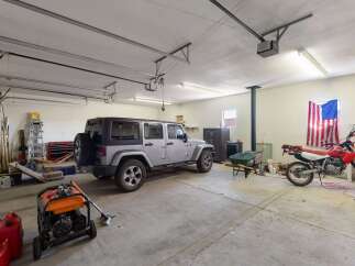 This spacious garage offers ample room for multiple vehicles, including a Jeep and motorcycles, alongside various tools and equipment like a generator and wheelbarrow.