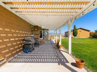 Enjoy outdoor living under this expansive white pergola, offering dappled shade over a concrete patio.