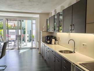 This modern kitchen features sleek, dark wood cabinetry and a spacious white countertop with an integrated sink.