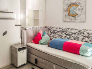 Discover this cozy bedroom featuring a comfortable bed with a vibrant bolster pillow and decorative cushions.
