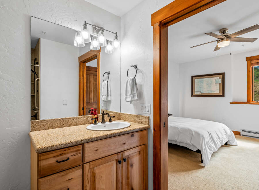 This charming bathroom features a granite countertop vanity with a wooden cabinet base, complemented by a large mirror with a vanity light fixture.
