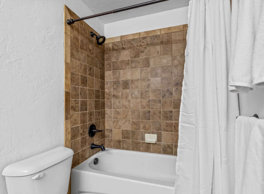 This bathroom features a classic white bathtub with a dark bronze faucet and showerhead, complemented by warm-toned tiled walls.