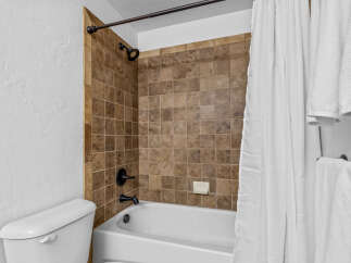 This bathroom features a classic white bathtub with a dark bronze faucet and showerhead, complemented by warm-toned tiled walls.