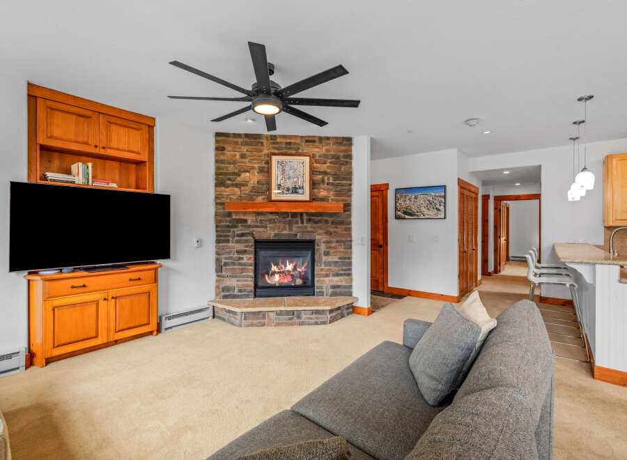 Cozy living room featuring a stone fireplace with a wooden mantel and a large flat-screen TV.