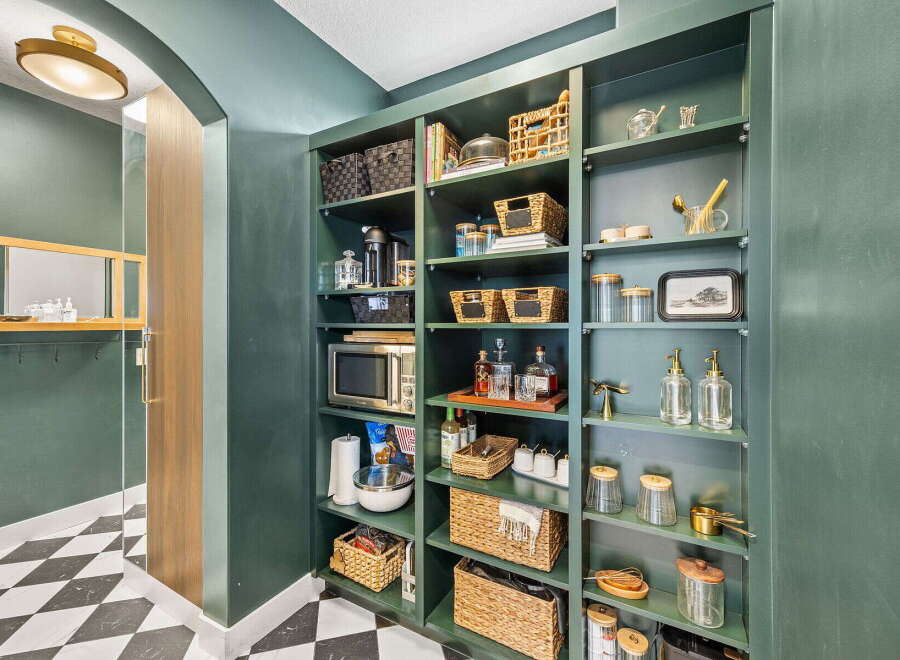 Discover the ultimate pantry organization with this beautifully designed space, featuring deep green shelving stocked with a variety of baskets, jars, and appliances.