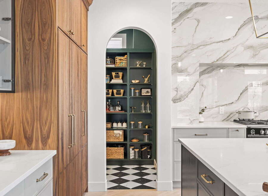 Discover this stunning kitchen featuring a spacious walk-in pantry with dark green shelving and a classic black and white checkered floor.