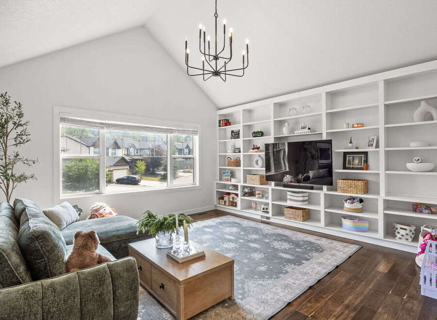 This spacious living room features a vaulted ceiling with a modern chandelier, complemented by a large window offering scenic views.