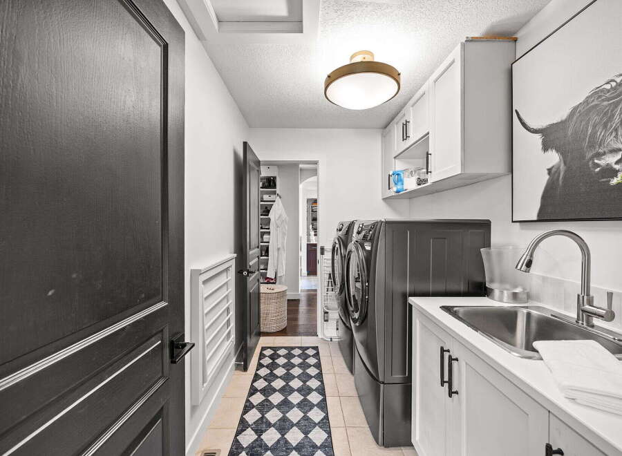 This spacious laundry room features a modern aesthetic with sleek white cabinetry and dark hardware.