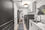 This spacious laundry room features a modern aesthetic with sleek white cabinetry and dark hardware.