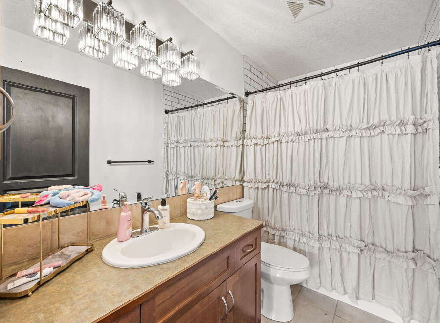This bathroom features a modern vanity with a sleek countertop and a deep sink, complemented by a stylish crystal chandelier light fixture.